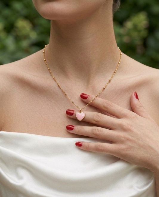 Woman wearing a gold necklace with a heart-shaped pink pendant, against a blurred green background.