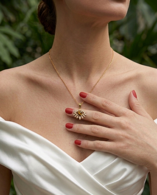 Woman wearing a gold necklace with a pendant, set against a blurred natural background.