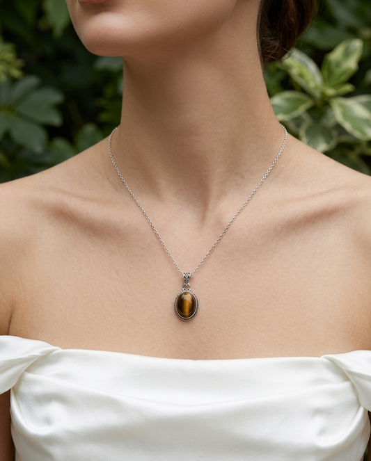 Necklace with a tiger's eye pendant worn by a person in a white dress against a green leafy background