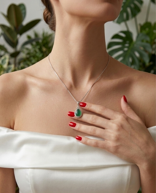 Woman wearing a necklace with a green pendant, set against a blurred natural background.