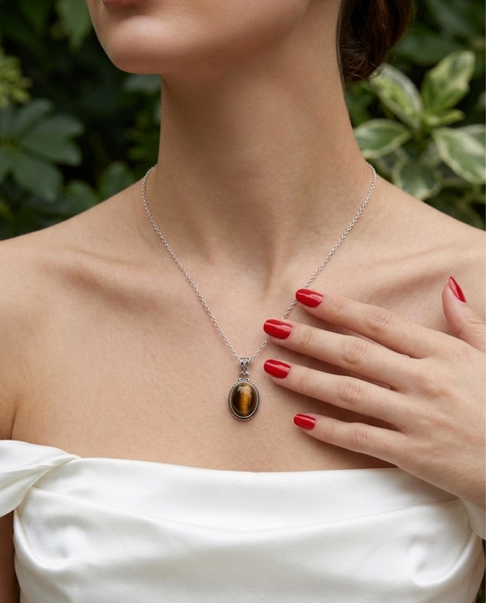 Woman wearing a silver necklace with a tiger's eye pendant, outdoors.