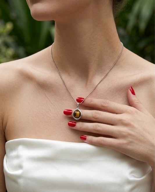 Woman wearing a necklace with a pendant, hand touching chest, blurred green background