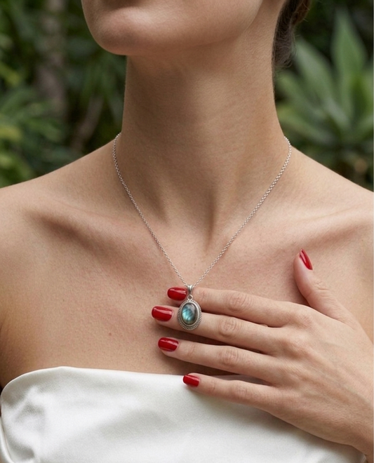 Woman wearing a silver necklace with a turquoise pendant, against a blurred natural background.