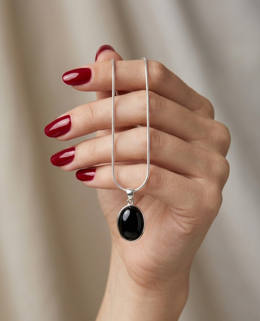 Hand holding a silver necklace with a black pendant against a neutral background