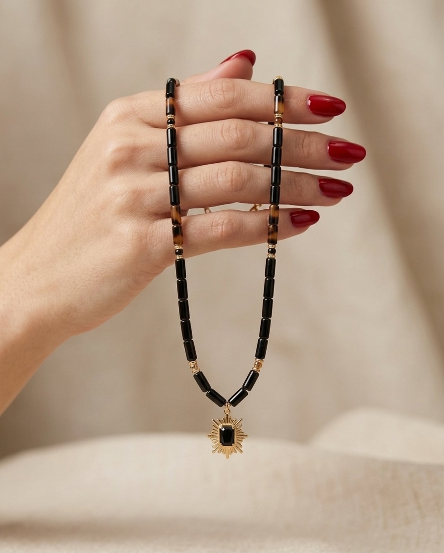 Hand holding a black beaded necklace with a sun pendant on a beige background