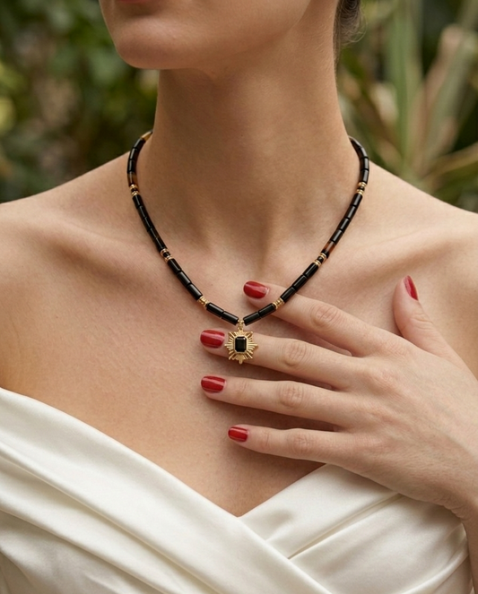 Woman wearing a black and gold beaded necklace with a white top.