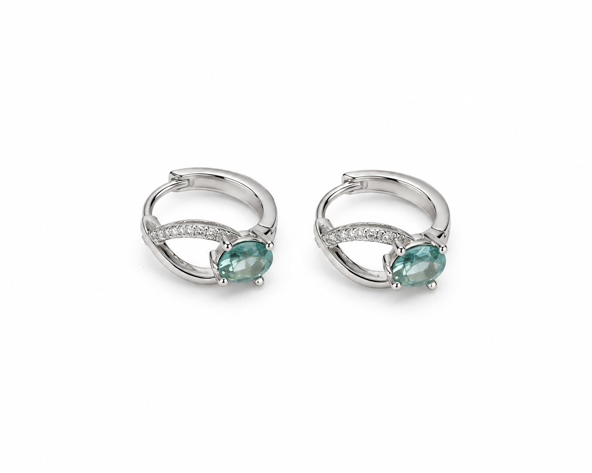 A pair of silver huggie hoop earrings with oval green gemstones and small clear accent stones, shown on a plain white background.