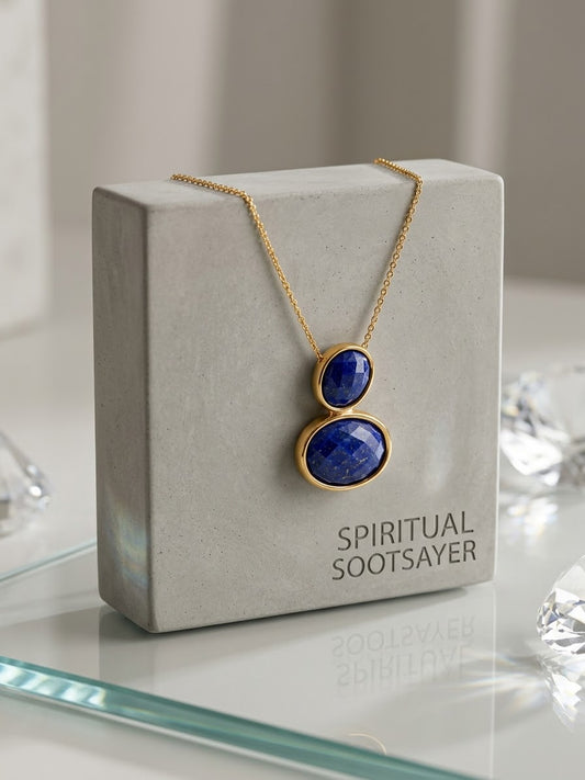 A gold necklace with two stacked oval lapis lazuli stones displayed on a gray jewelry box labeled 'SPIRITUAL SOOTSAYER'.