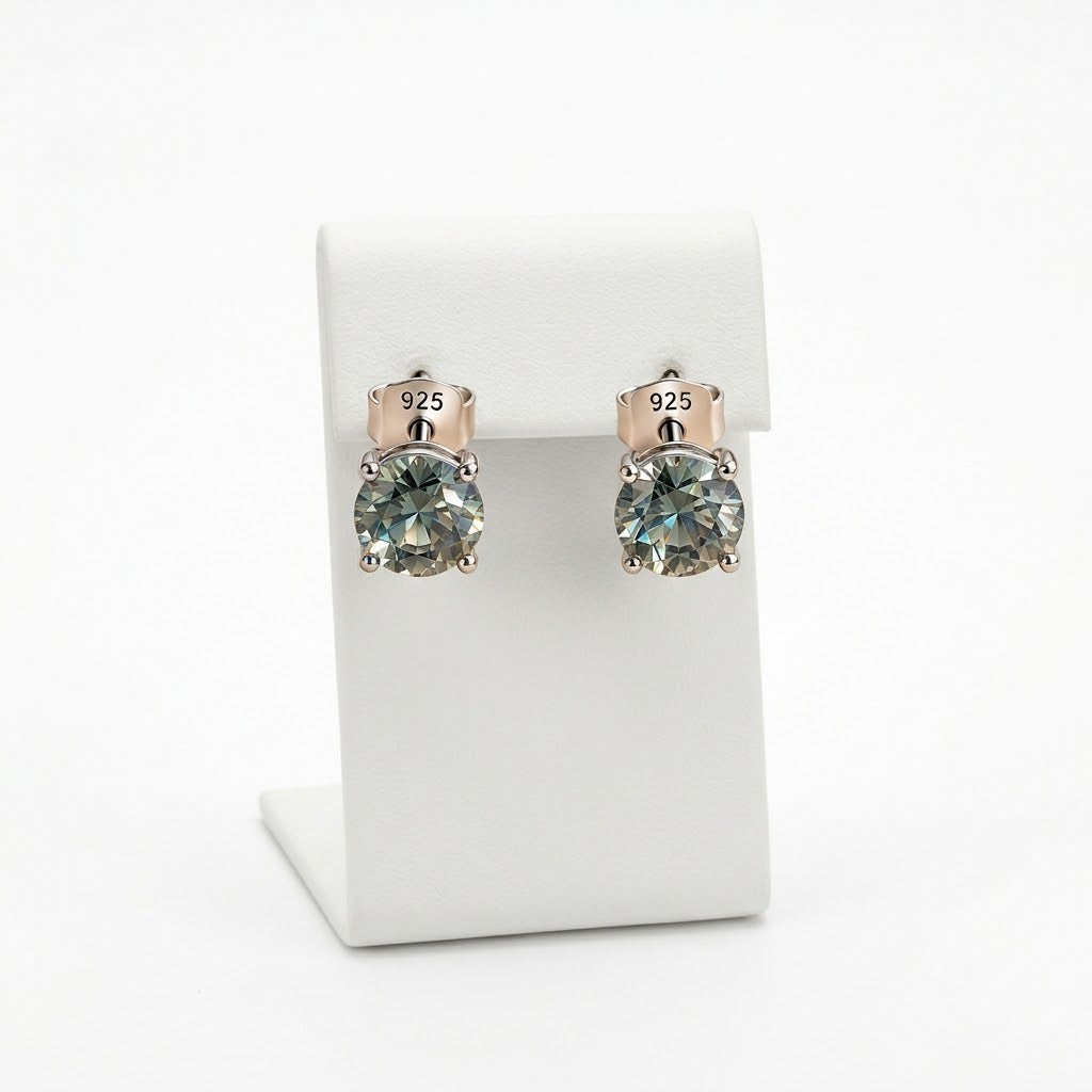 A pair of stud earrings with round iridescent gray-green gemstones in a silver-toned setting, displayed on a white jewelry stand. The back of the earrings is rose gold-toned with a '925' sterling silver mark.
