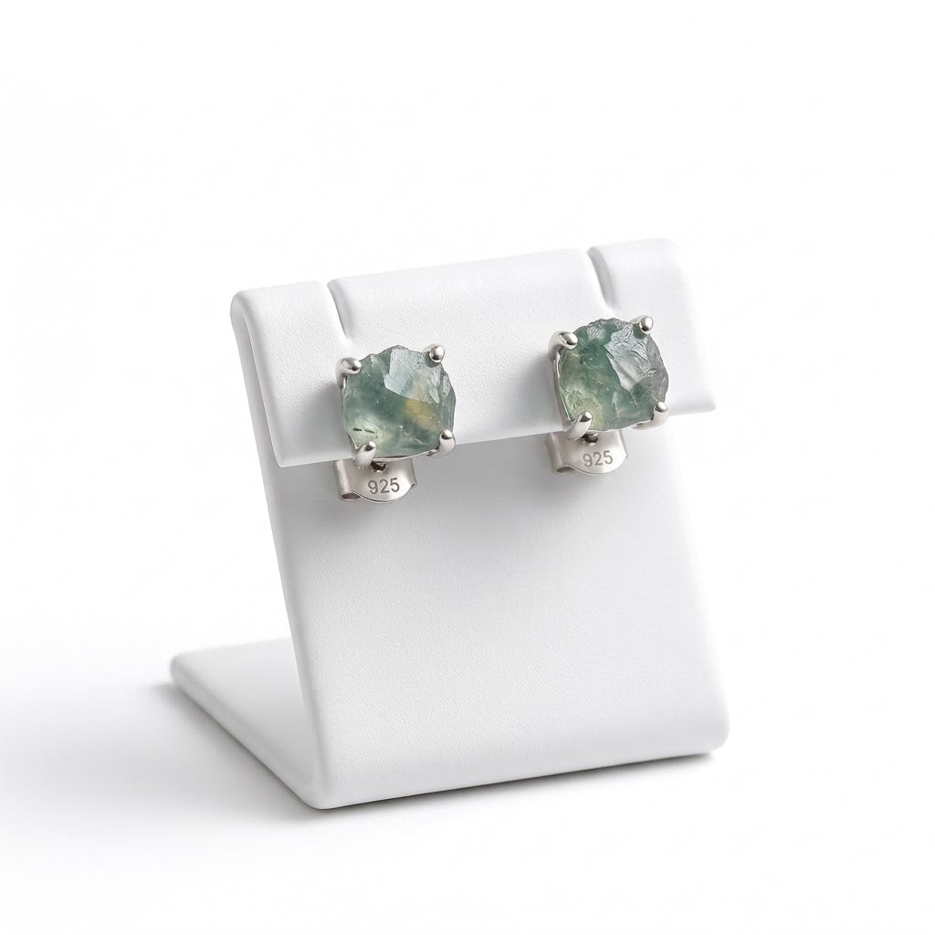 A pair of square-cut green gemstone stud earrings in silver settings, displayed on a white jewelry stand against a white background.