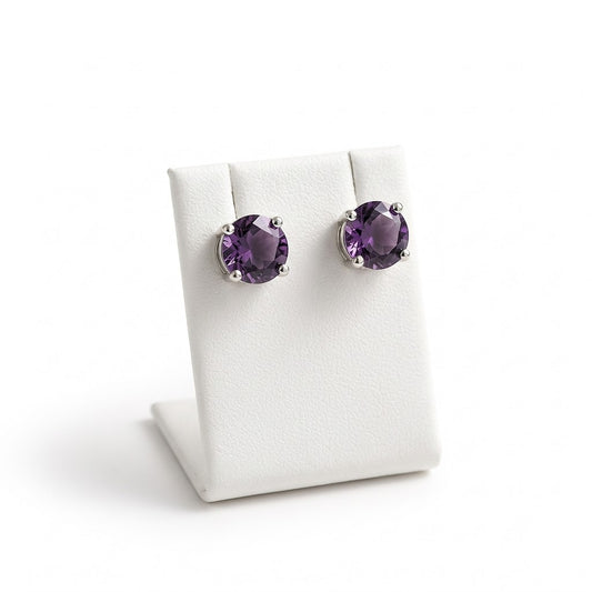 A pair of oval purple gemstone stud earrings in silver prong settings, displayed on a white jewelry stand against a white background.