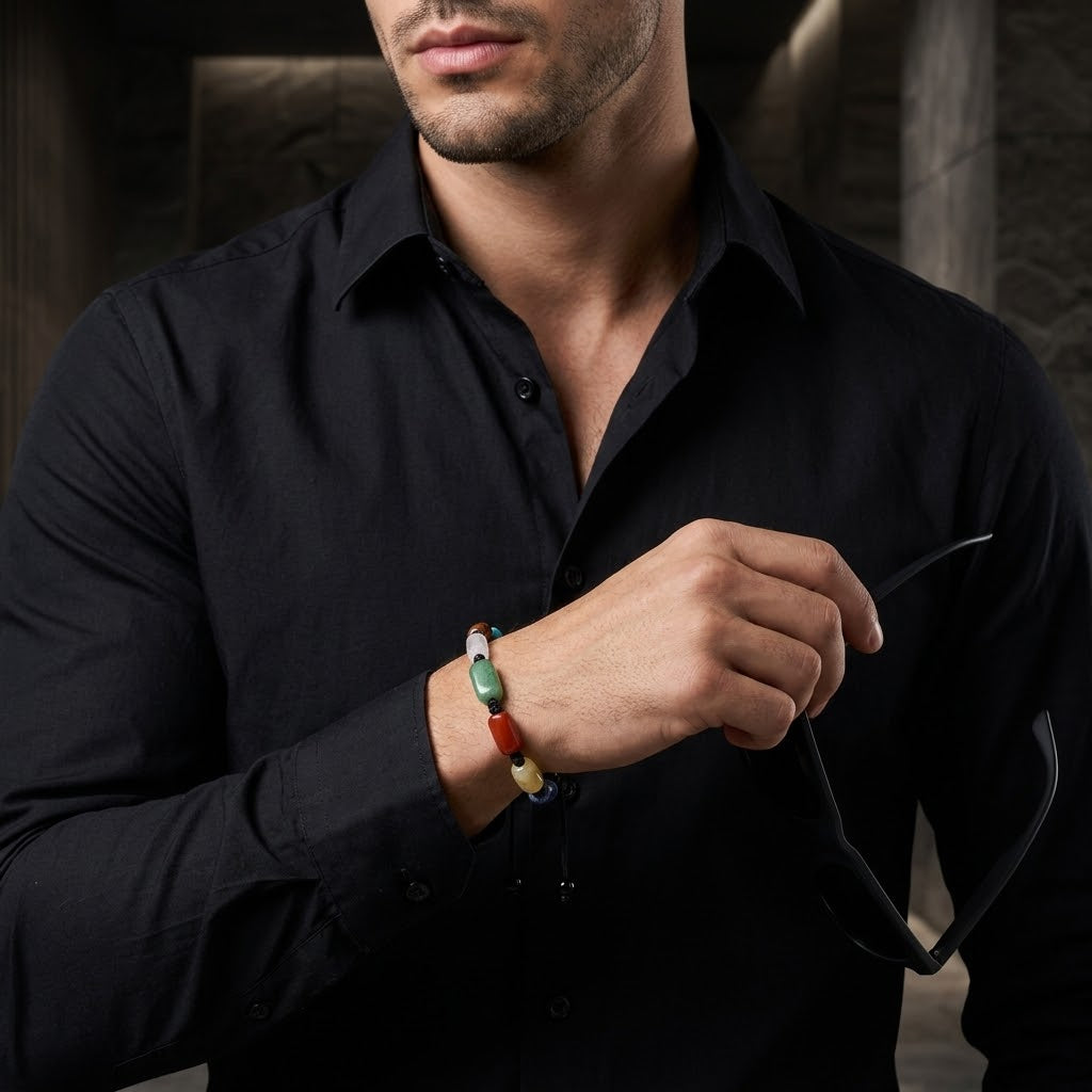 A man wearing a black button-down shirt and holding black sunglasses while adjusting a colorful beaded bracelet on his wrist.