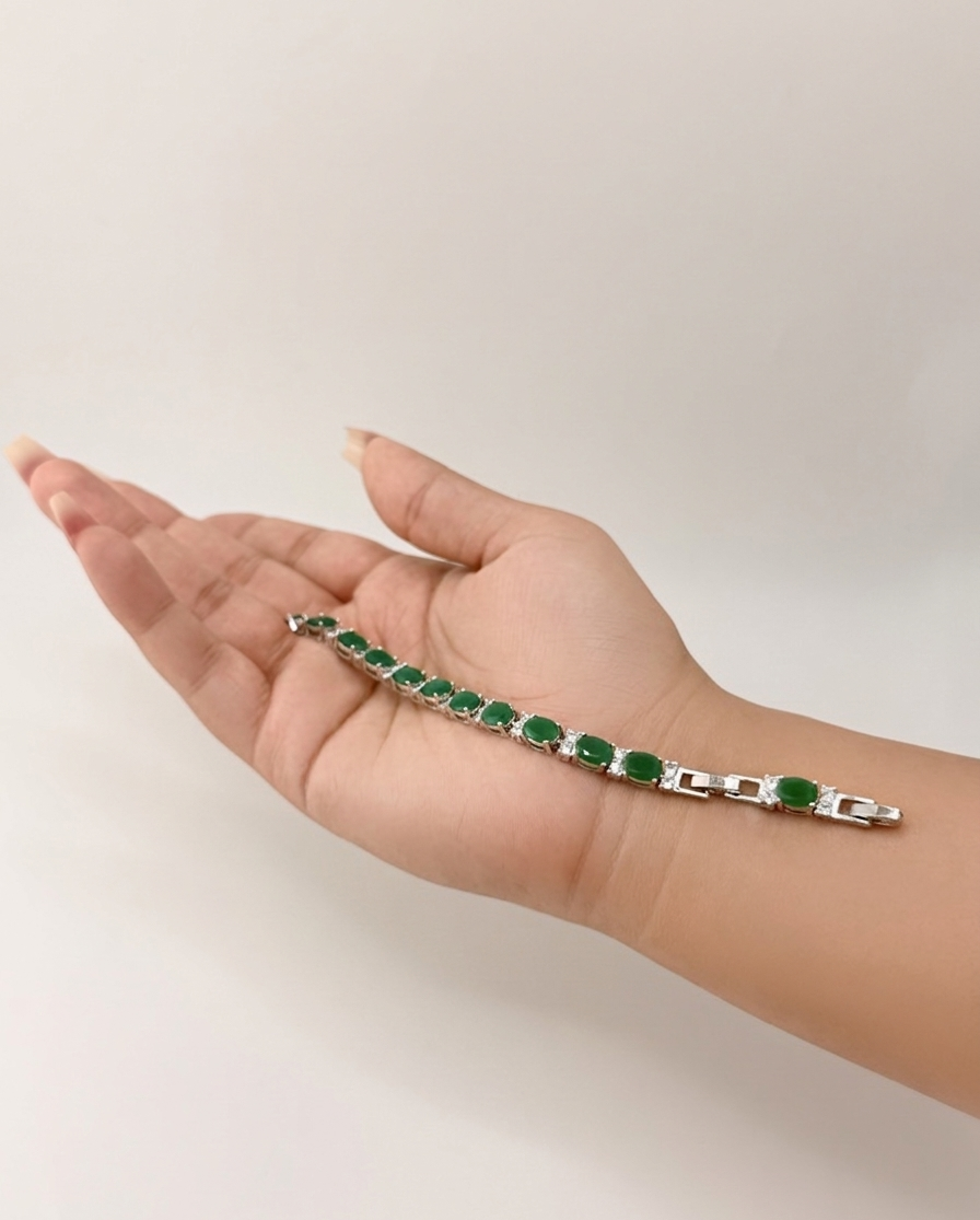 Hand wearing a silver bracelet with green gemstones on a plain background