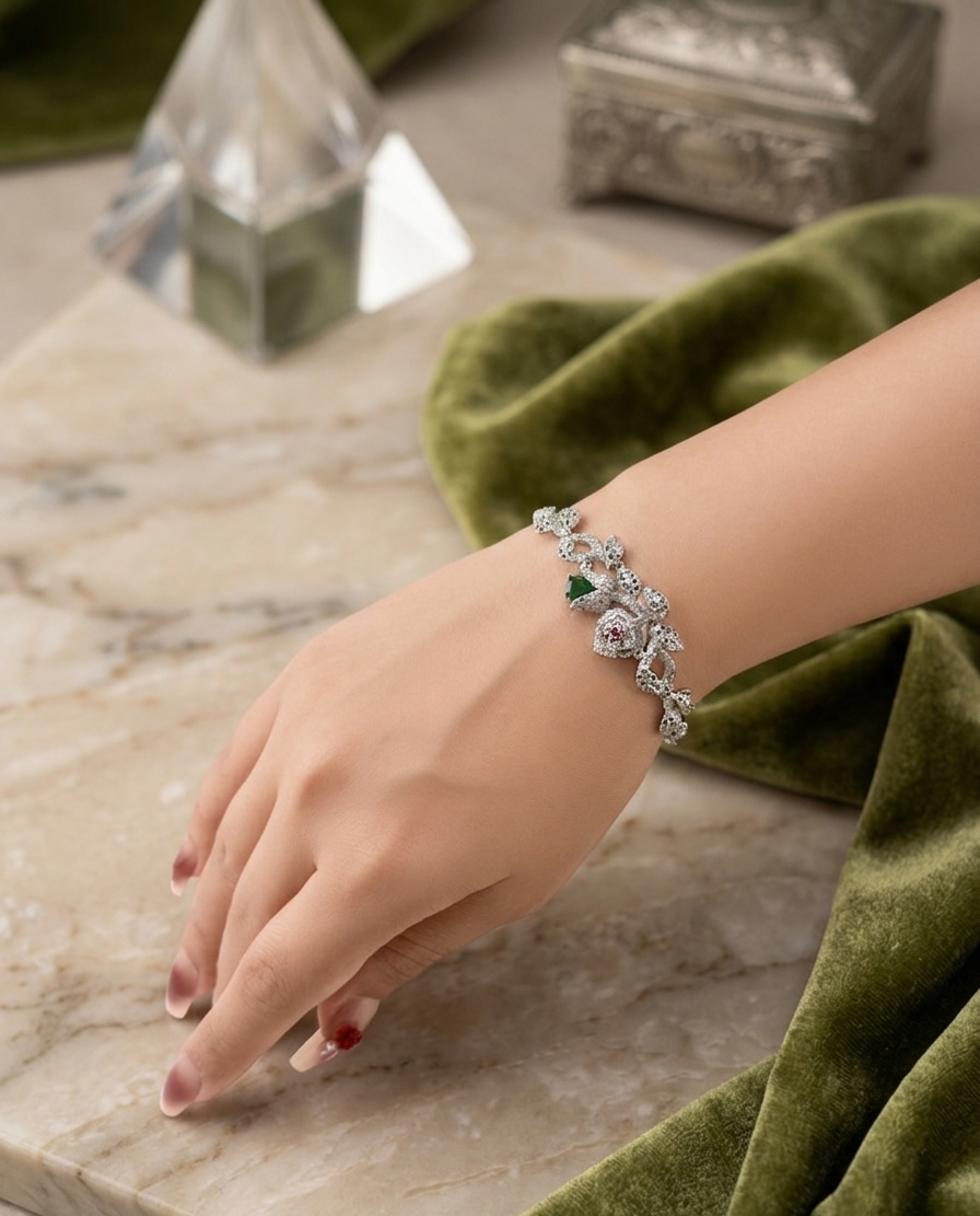 Hand wearing a silver bracelet with green gemstones on a marble surface with green fabric.