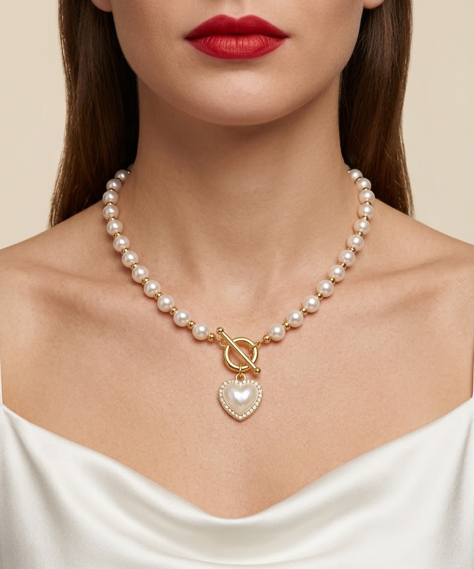 A close-up of a model wearing a pearl necklace with gold-toned beads, a toggle clasp, and a heart-shaped pearl pendant.