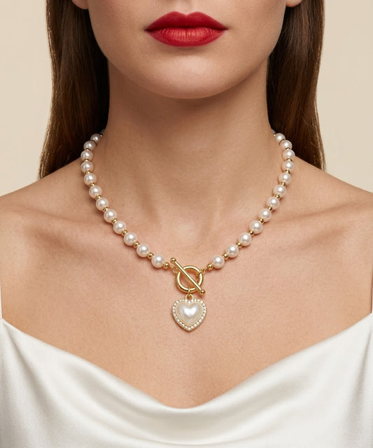 A close-up of a model wearing a pearl necklace with gold-toned beads, a toggle clasp, and a heart-shaped pearl pendant.