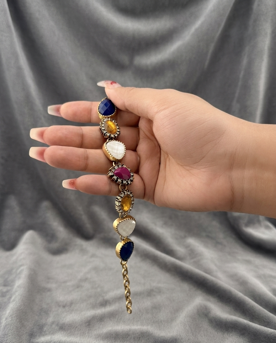 Hand holding a decorative bracelet with colorful stones against a gray fabric background