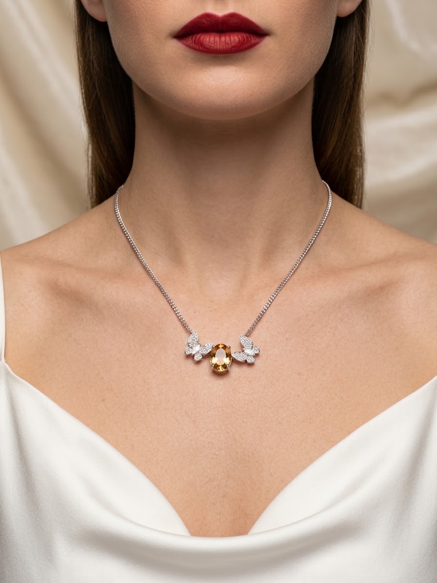 A close-up of a model wearing a delicate silver chain necklace with a central pendant featuring a small yellow gemstone and two white flower-like charms, styled with a white top and red lipstick.