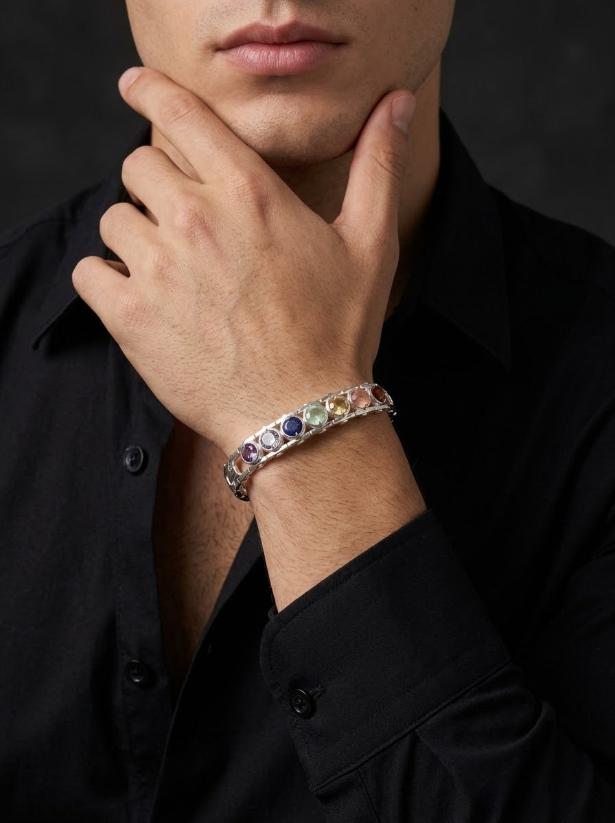 A close-up of a man wearing a silver-toned bracelet with colorful gemstones, paired with a black button-down shirt against a dark background.