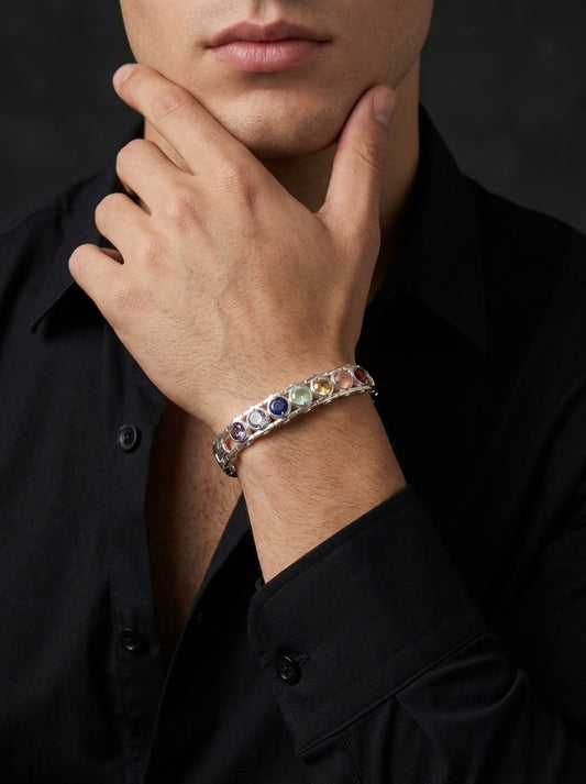 A close-up of a man wearing a silver-toned bracelet with colorful gemstones, paired with a black button-down shirt against a dark background.