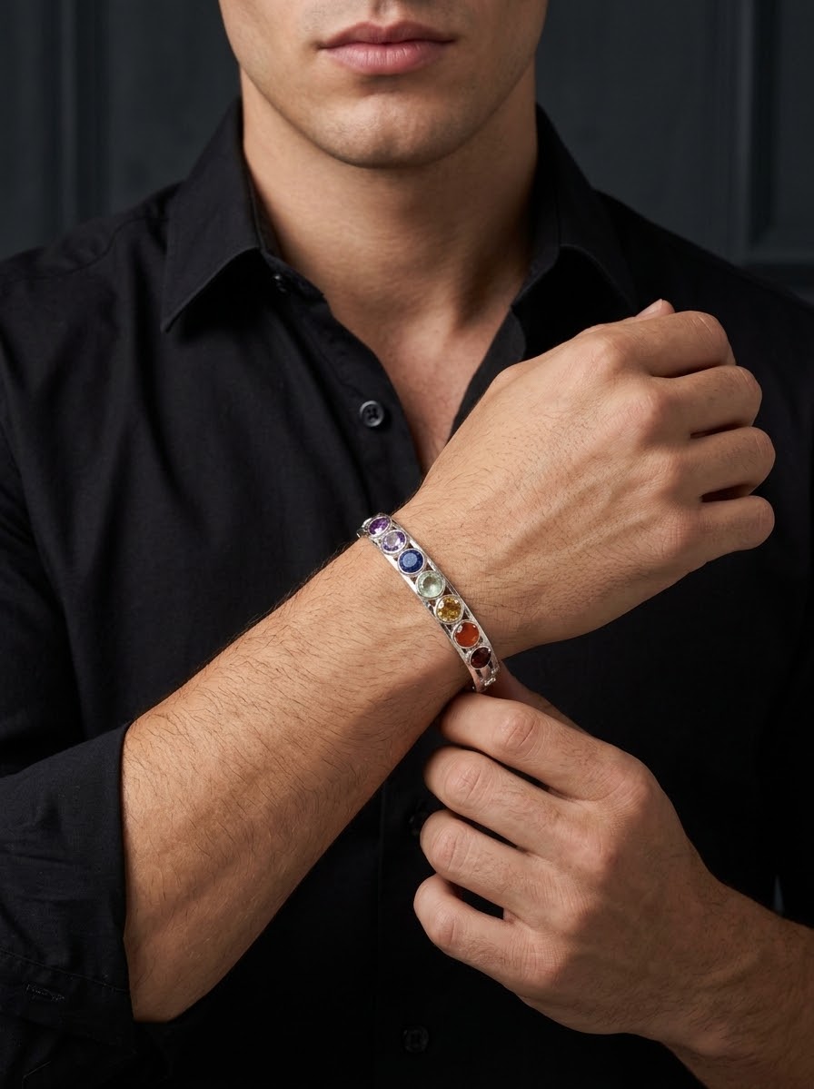 A close-up of a man wearing a silver-toned cuff bracelet with multiple colorful gemstones, shown against a dark background.