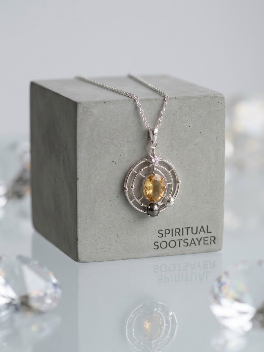 A silver-toned Spiritual Sootsayer pendant necklace with a yellow crystal, displayed on a gray concrete block.