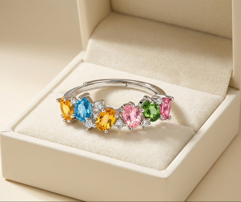A silver-toned cuff bracelet with five colorful marquise-cut gemstones in yellow, blue, pink, green, and orange, displayed in an open cream-colored jewelry box.