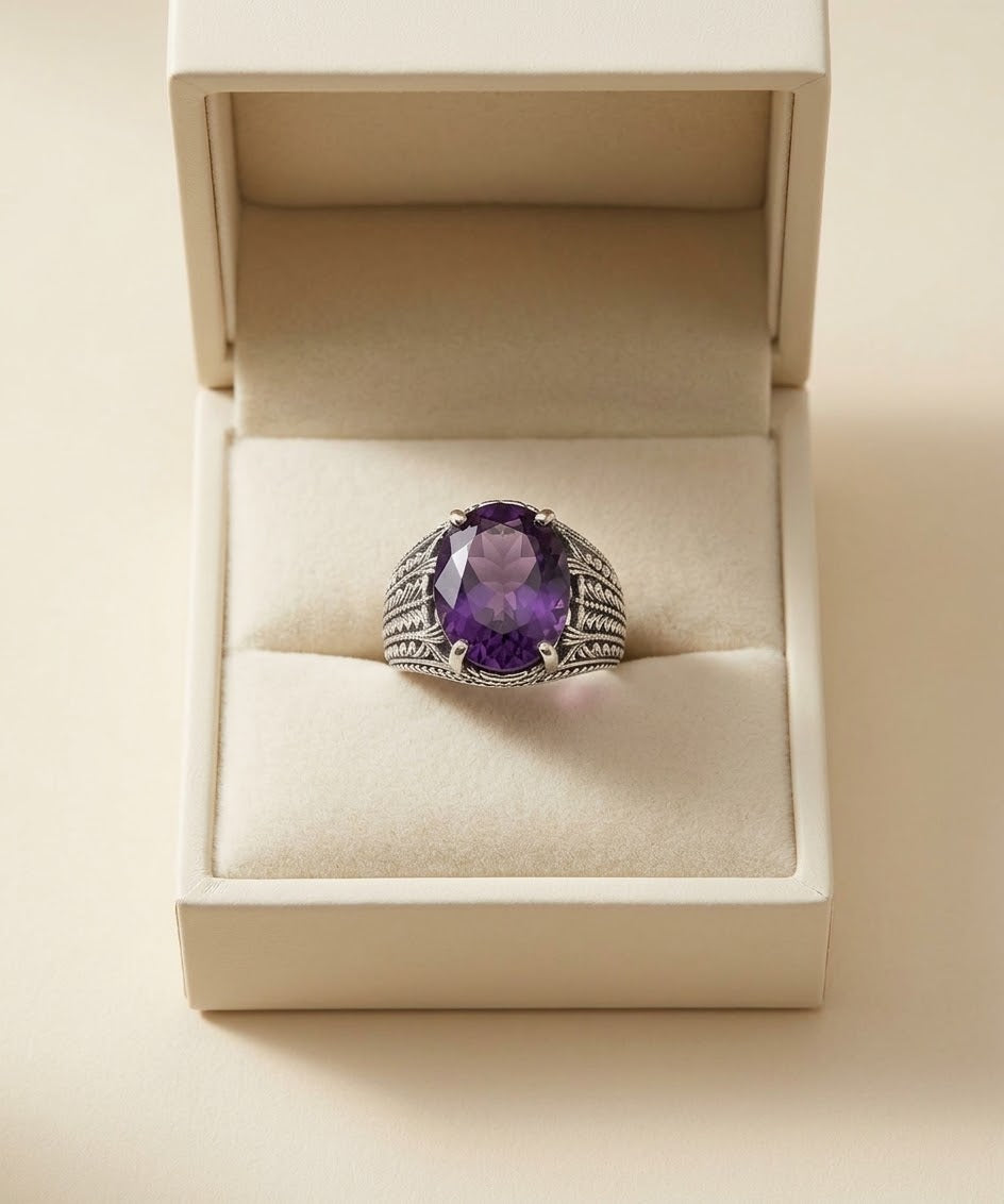A silver-toned ring with a large oval purple amethyst center stone, displayed in an open cream-colored jewelry box on a beige background.