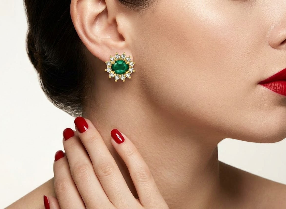 A close-up of a woman wearing a green oval emerald stud earring with a halo of small clear stones, shown against a clean light background.