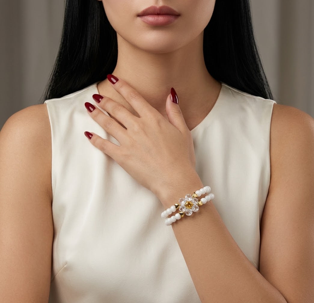 A close-up of a woman wearing a pearl beaded bracelet with a central floral cluster featuring a yellow gemstone and clear stones, paired with a cream satin top.