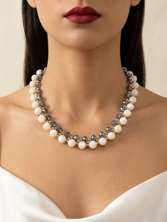 A close-up of a model wearing a double-strand pearl and gray stone beaded necklace with gold-toned metal links, paired with a white satin top.