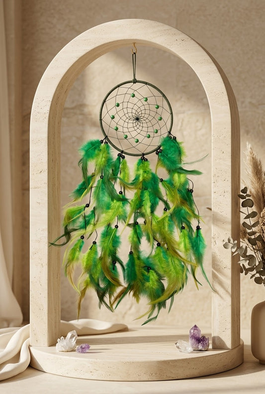 A green dreamcatcher with hanging feathers displayed inside a large beige arched wooden frame on a tabletop, with small crystals and dried grass nearby.