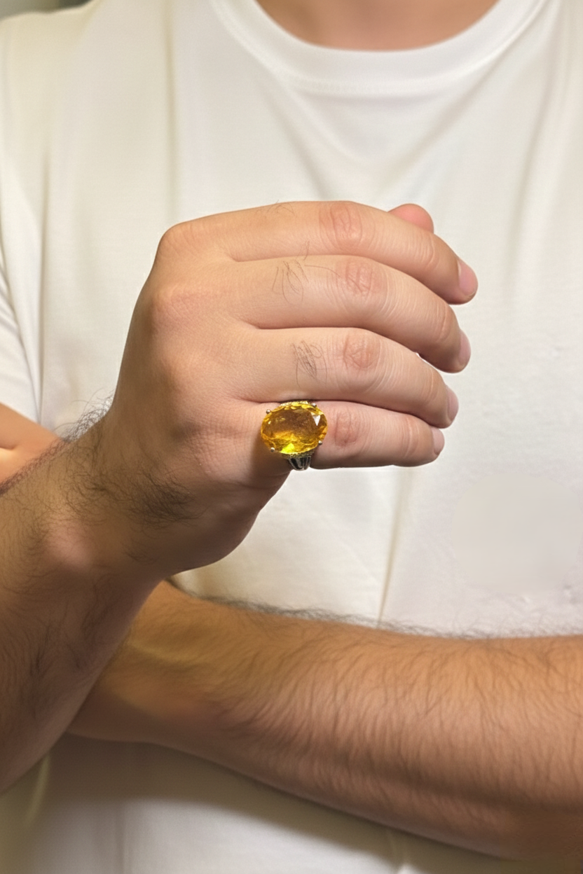 Hand wearing a large yellow gemstone ring against a white shirt background