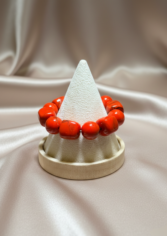 Red beaded bracelet on a white cone-shaped jewelry stand against a beige fabric background