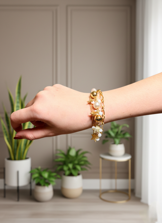 Hand wearing a gold bracelet with pearls in a room with plants
