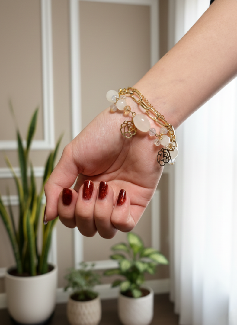 Hand with red nail polish wearing a gold bracelet in a room with plants