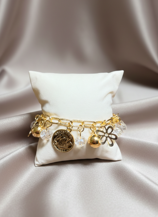 Gold bracelet with charms on a white pillow against a beige fabric background