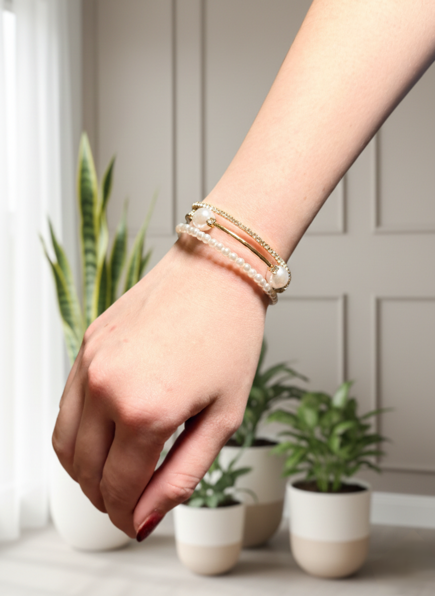 Hand wearing multiple bracelets with plants in the background