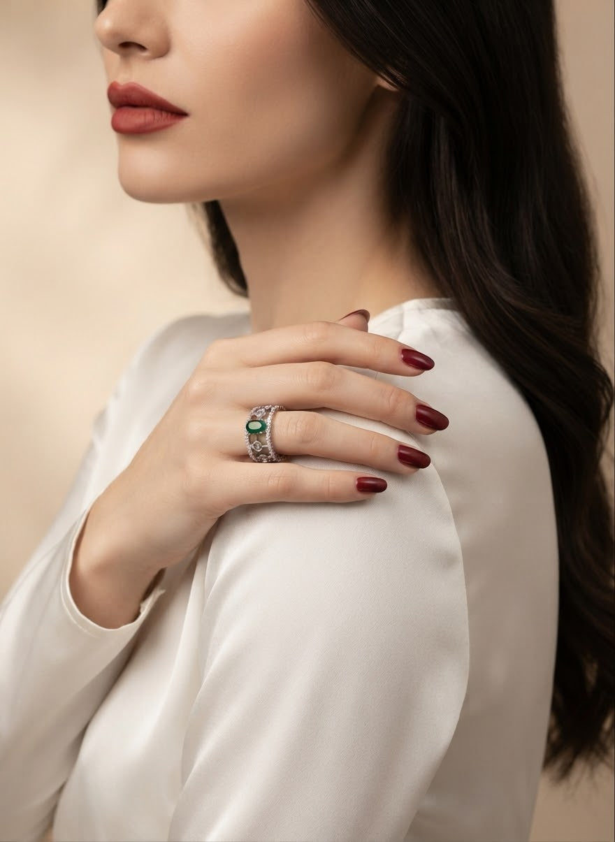 A close-up lifestyle shot of a woman wearing a silver ring with a green emerald center stone, resting her hand on her shoulder.