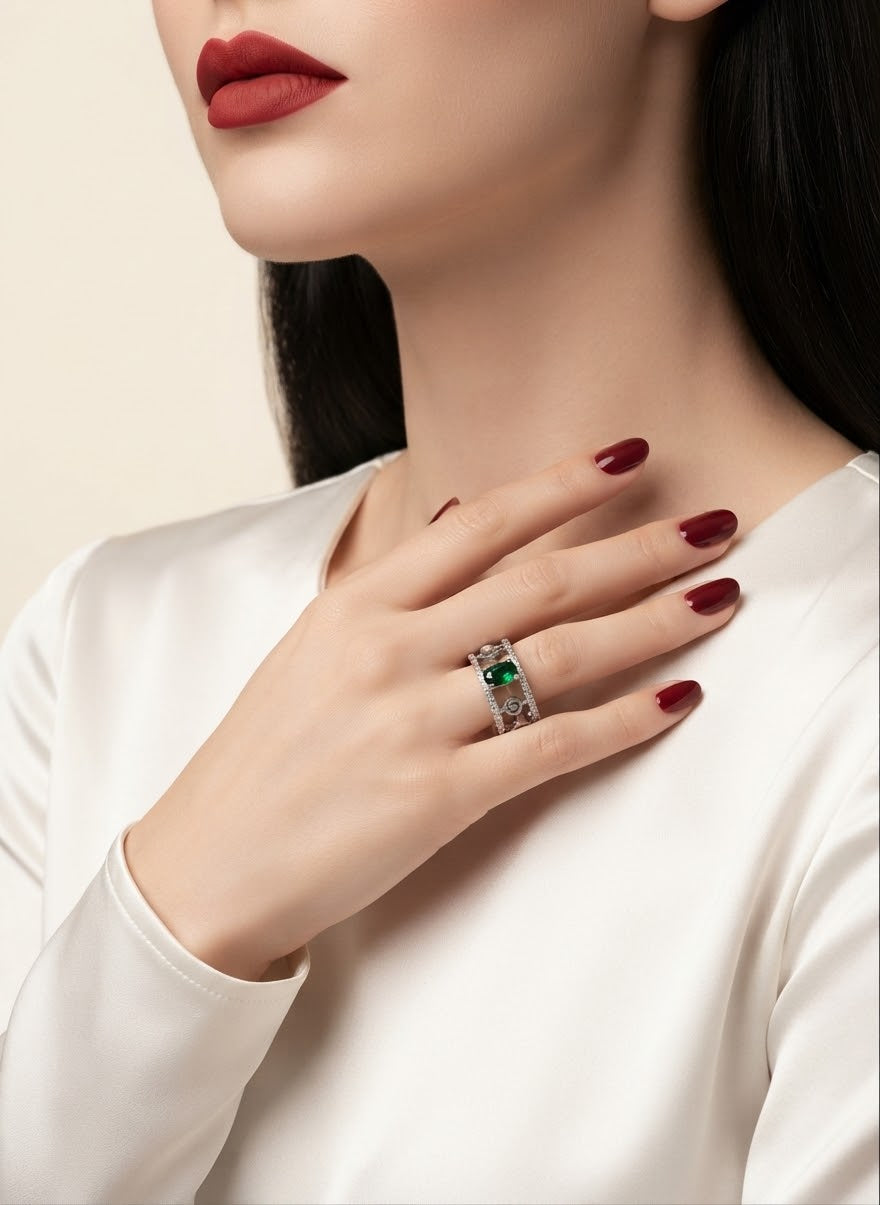 A close-up lifestyle shot of a model wearing a silver ring with a green rectangular stone and small clear stones, shown on her finger as she wears a white satin top.
