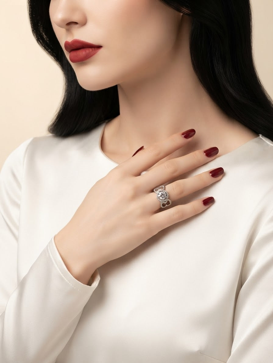 A close-up of a woman wearing a silver ring with clear stones on her finger, dressed in a white satin top against a soft beige background.