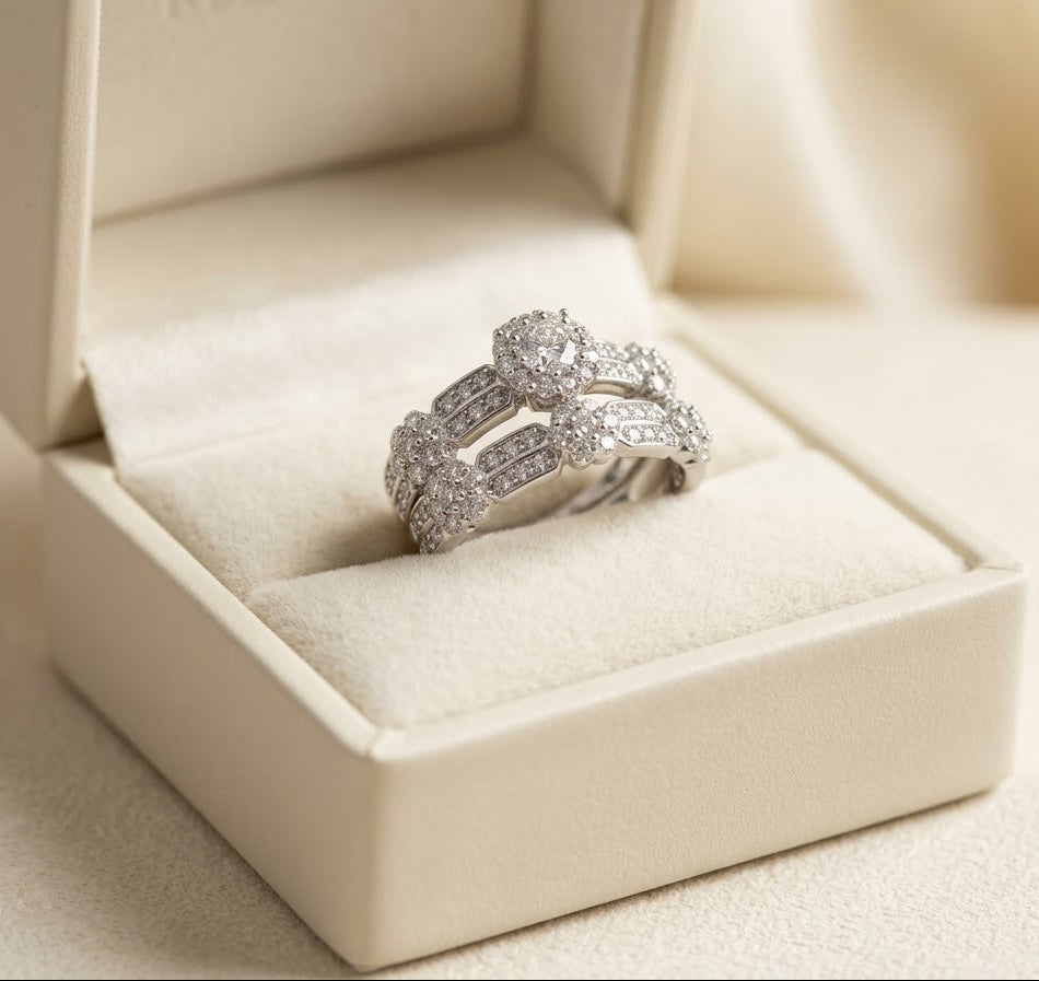 A silver-toned wedding band with a central round diamond and smaller side stones, displayed in an open cream-colored jewelry box.