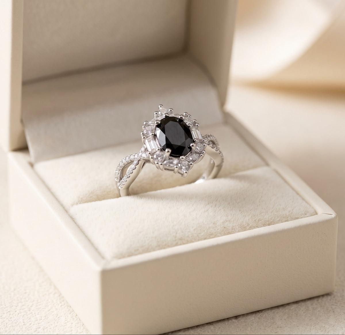 A silver ring with a round black center stone and small clear accent stones, displayed in an open cream-colored jewelry box.