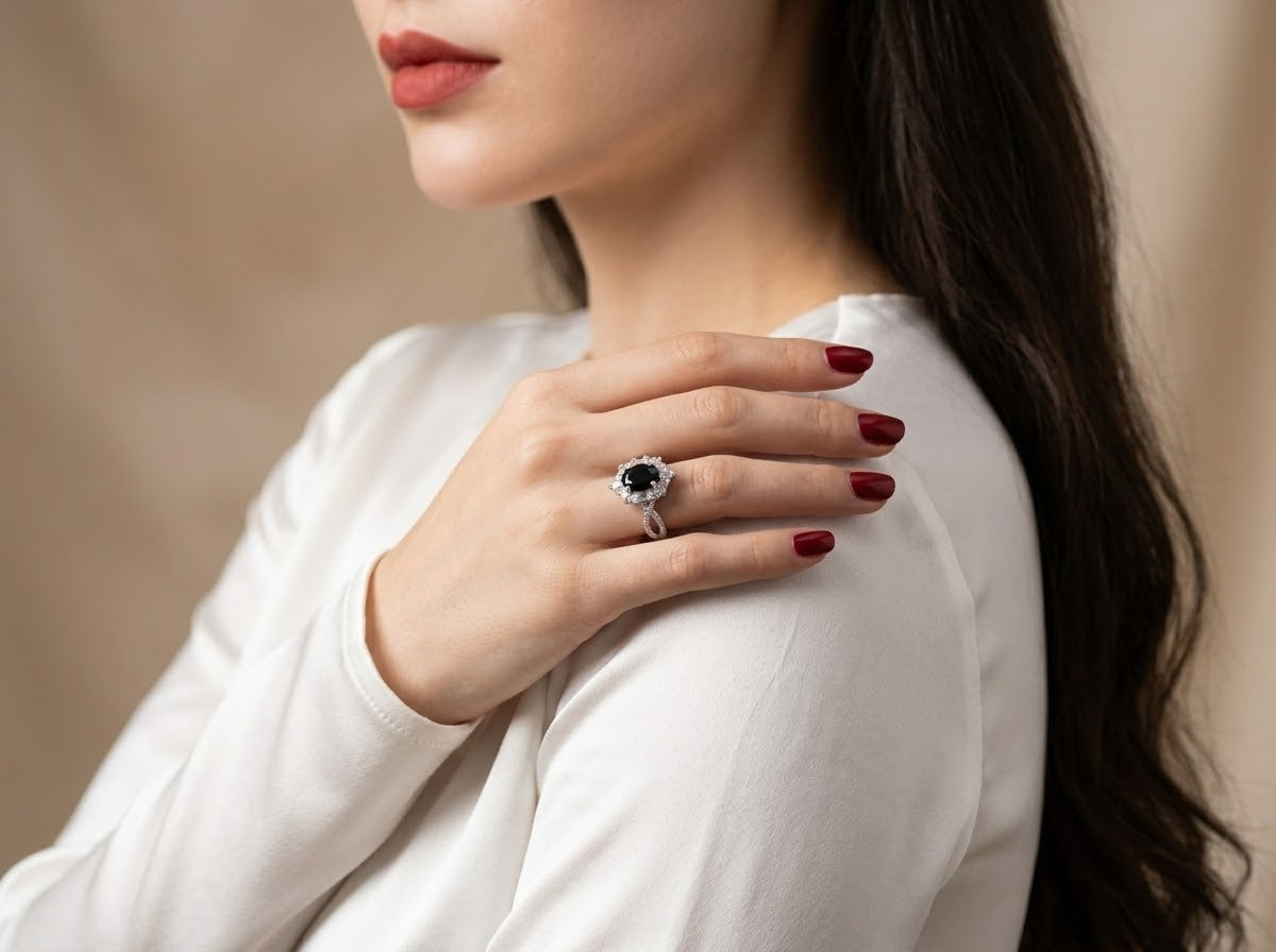 A close-up lifestyle shot of a woman wearing a silver ring with a dark oval gemstone, resting her hand on her shoulder.