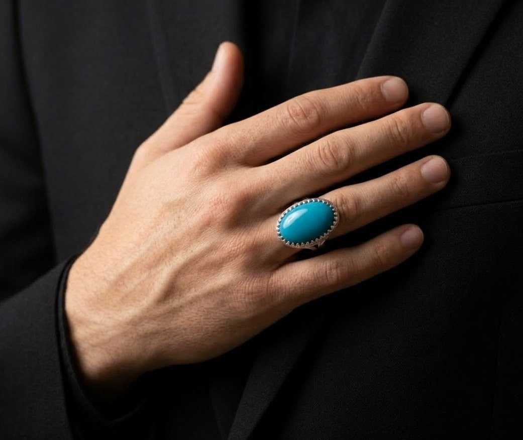 A close-up of a person's hand resting on a black suit jacket, wearing a silver ring with a large oval turquoise cabochon stone.