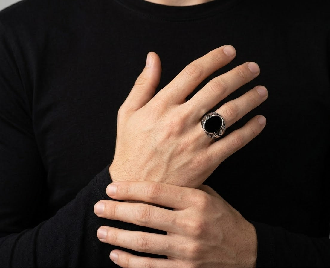 A close-up of a person wearing a large silver-toned ring with a black oval center, shown on their hand against a black long-sleeve shirt.