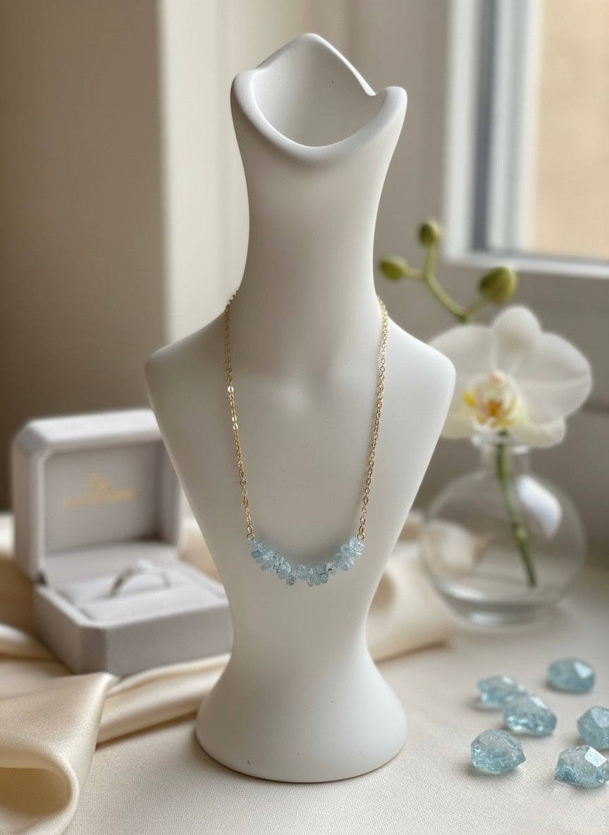 Necklace with blue stones displayed on a white mannequin bust, with a ring box and orchid in the background.