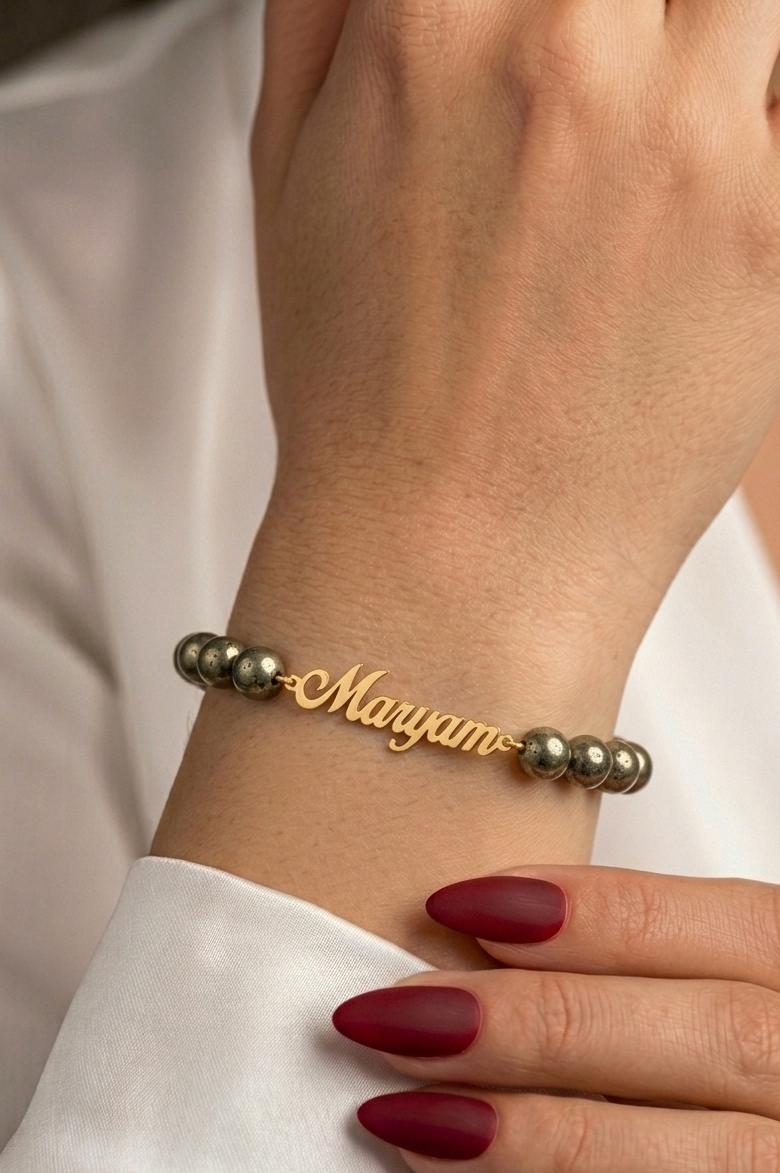 Gold bracelet with 'Maryam' on a wrist against a neutral background