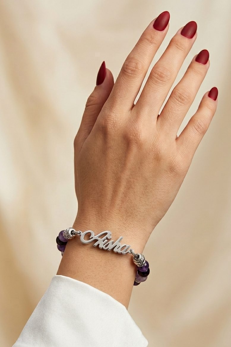Hand wearing a bracelet with 'Aisha' on a beige background