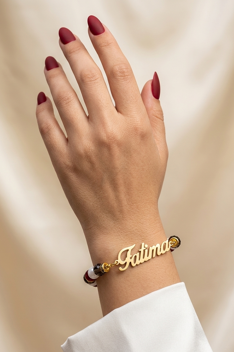 Hand wearing a gold bracelet with 'Fatima' on a beige background